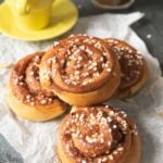 A pile of kanelbullar served with a cup of espresso and a tall glass of coffee.