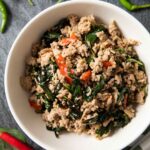 An overhead shot of a plate of Thai basil and ground pork, served with a bowl of rice.