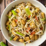 An overhead shot of a plate of stir-fried tofu and bean sprouts, served with a bowl of rice.