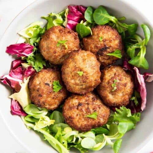 Six pieces of Norwegian pork patties, served on a bed of leafy greens.