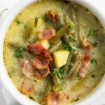 A serving of German green bean soup, highlighting the bits of vegetables and bacon in it.