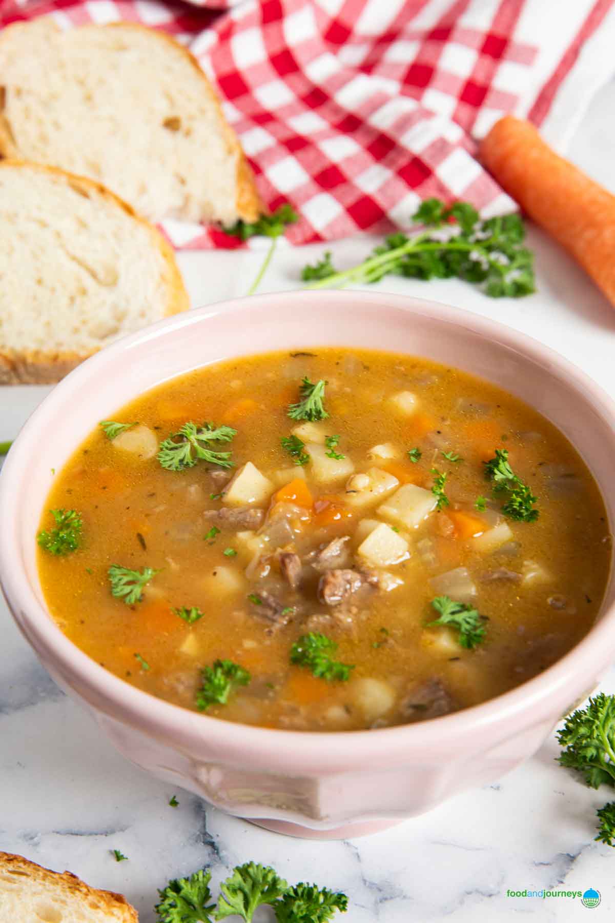 A bowl of soup with oxtail, in German style, served with slices of bread, and fresh carrot and parsley in the background.