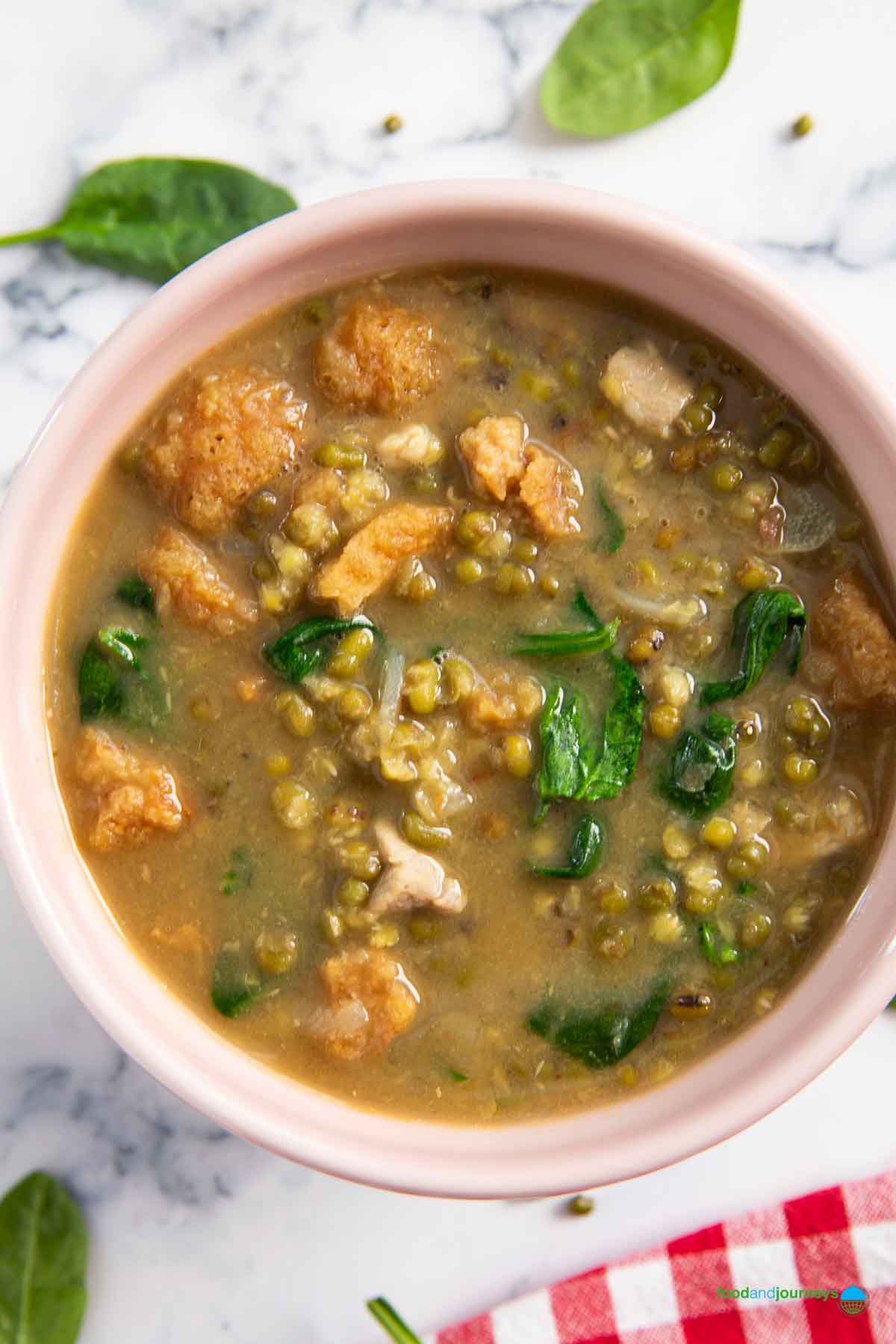 A bowl of Filipino mung bean soup, served with bits of chicharon, and some leafy greens around it.