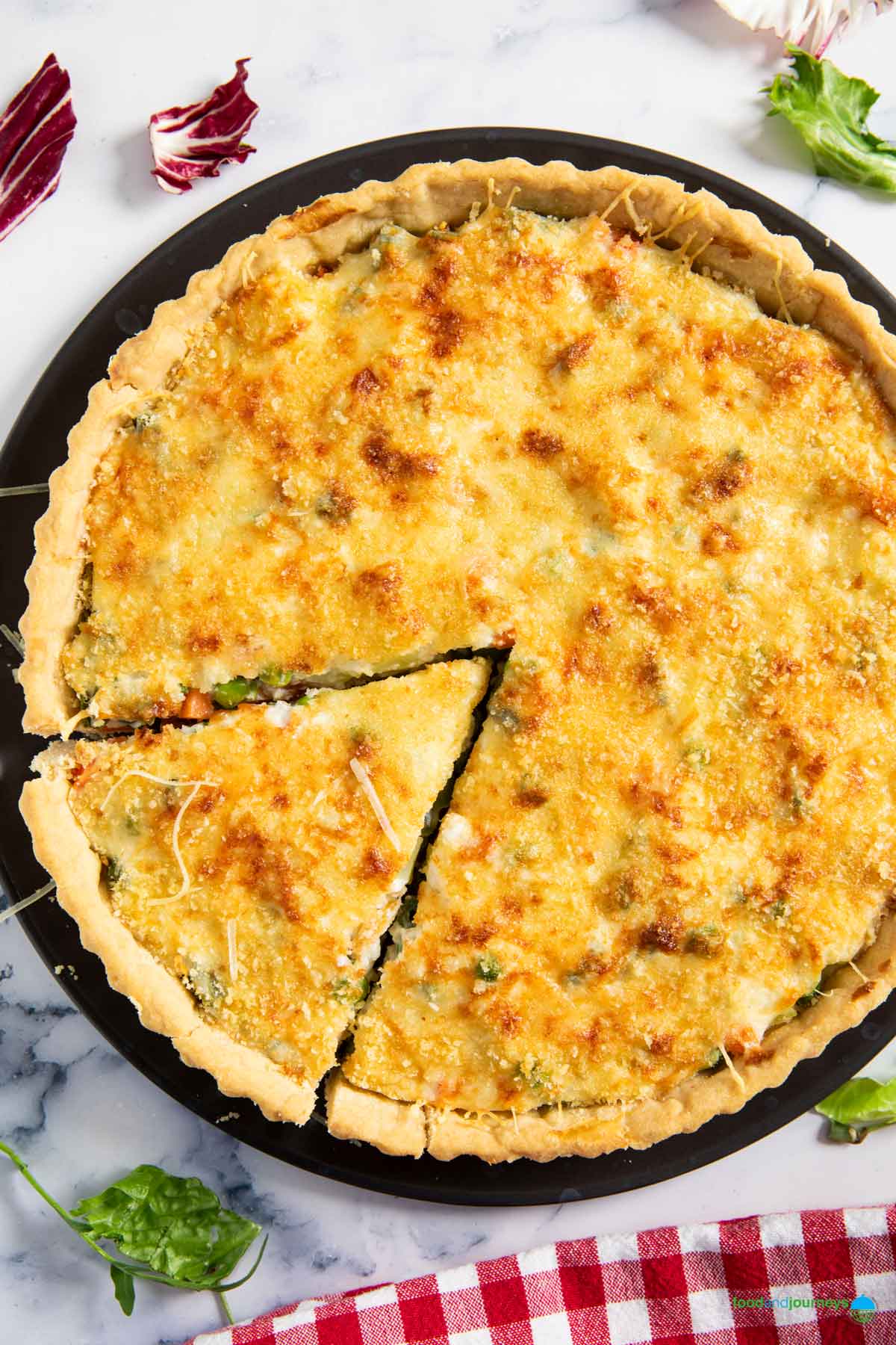 A freshly baked French vegetable tart, with a slice ready for serving, and bits of salad greens around it.