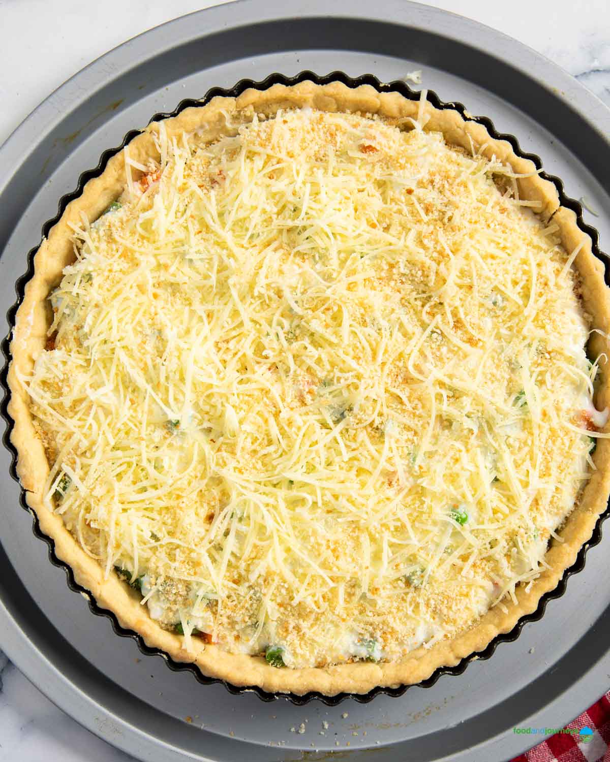 Adding breadcrumbs and grated cheese on top of summer vegetable tart before baking.