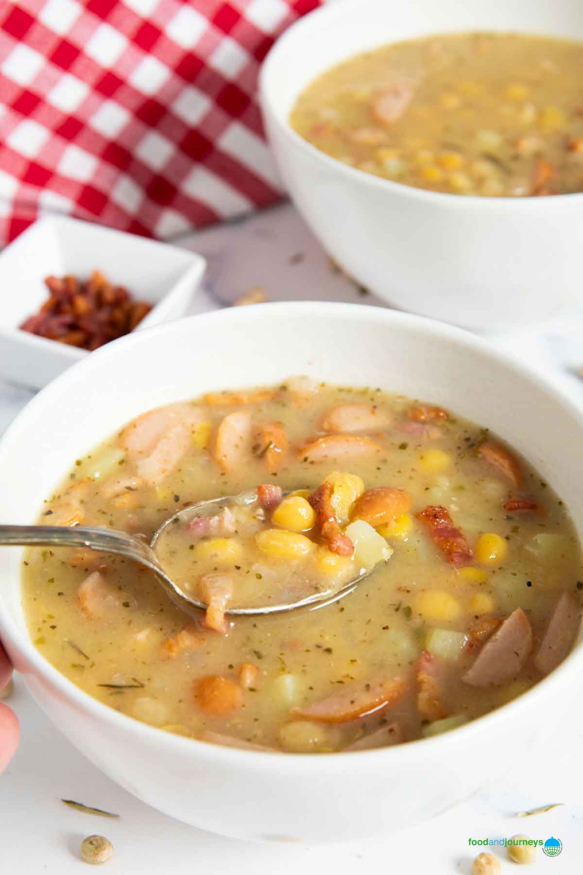 Two bowls of erbsensuppe served, with crunchy bacon bits in the background.