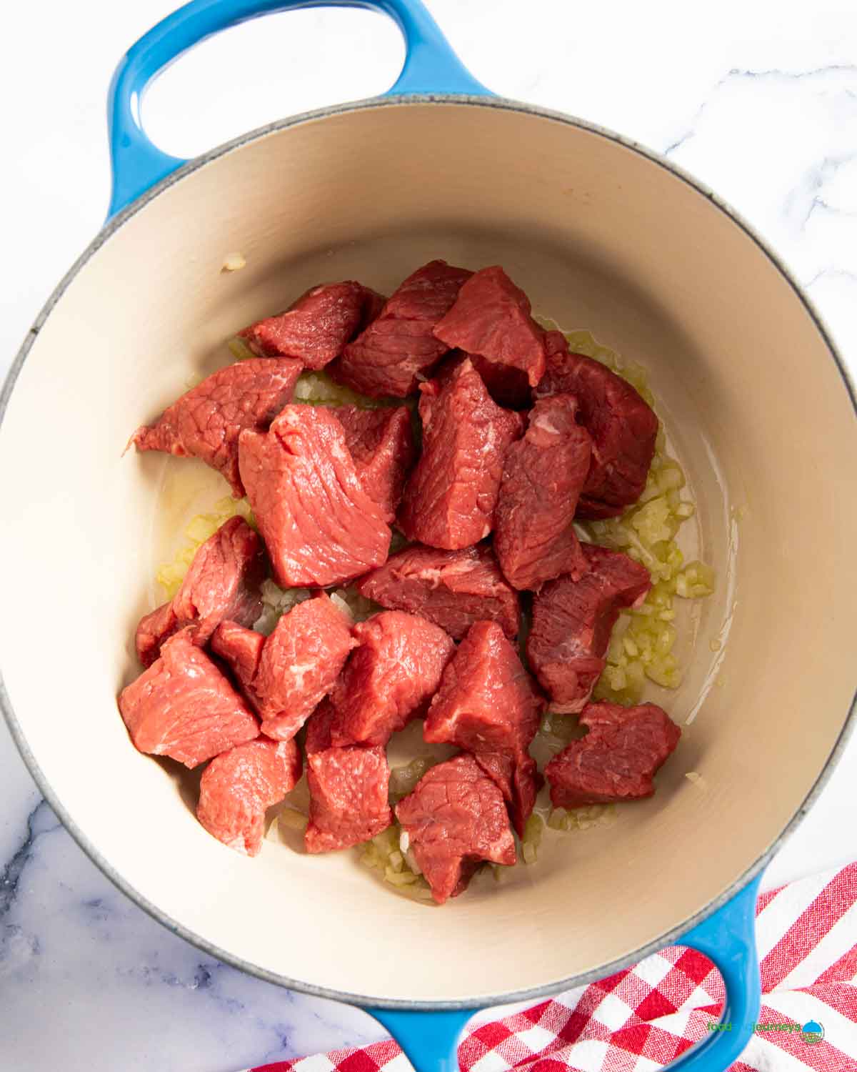 Adding the chunks of beef into the sautéed onion and garlic, to cook it a bit, before starting with the layering of flavor for the kaldereta sauce.
