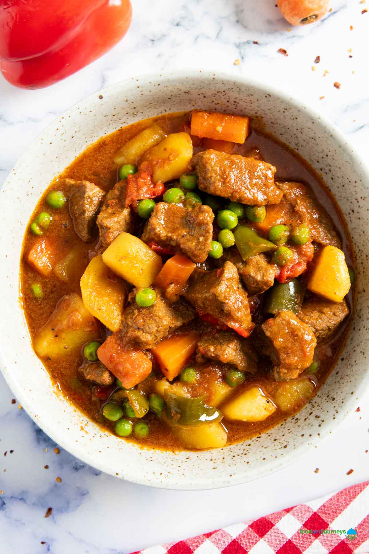 A plate of Filipino kaldereta with beef, with red pepper and carrot next to it.