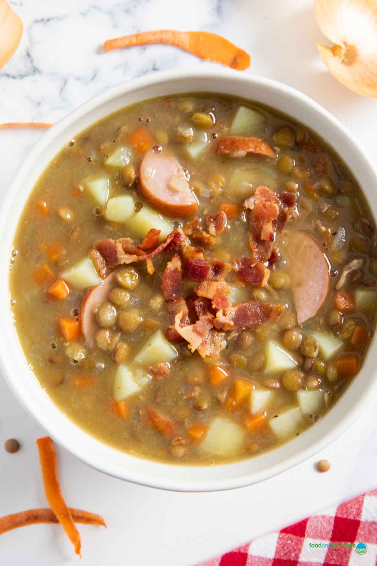 A serving of classic German lentil soup with carrot and onion peel in the background.