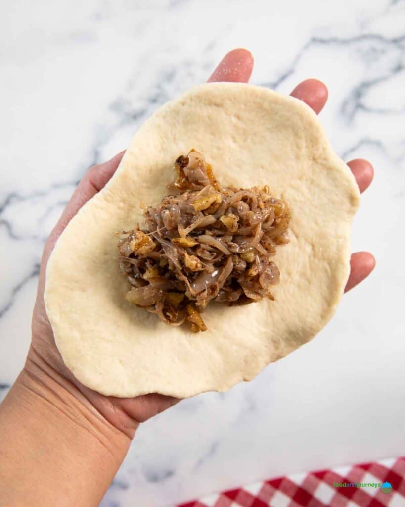 Assembling the Lebanese stuffed bread by placing the filling in the centre before folding the sides and forming it into a ball.
